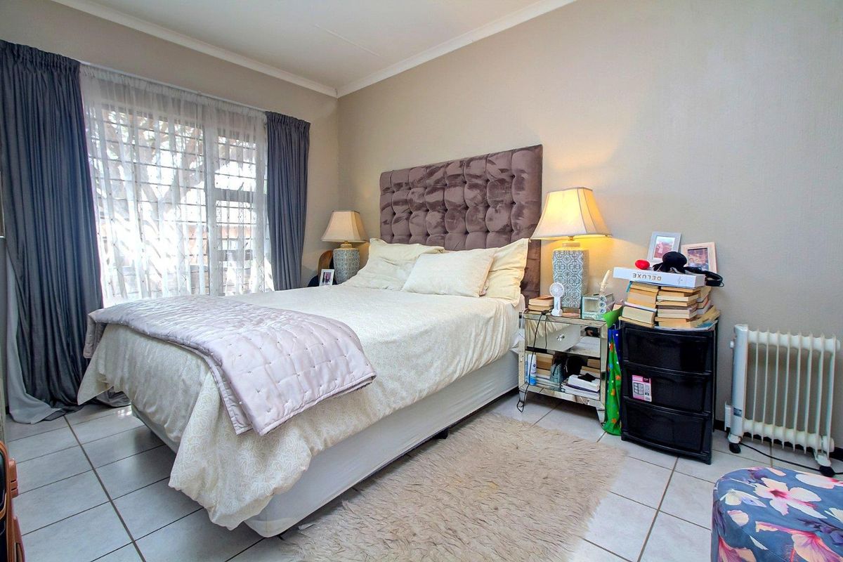 A well-lit bedroom featuring tiled flooring, neutral wall finishes, and a large window with curtain tracks.