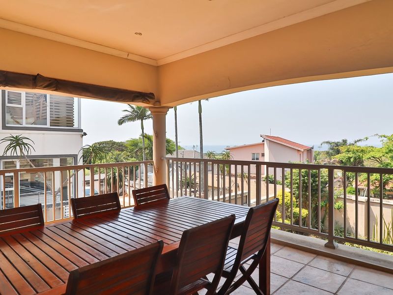 A spacious covered balcony featuring tiled flooring and a metal balustrade, offering an elevated outdoor area suitable for relaxation and dining.