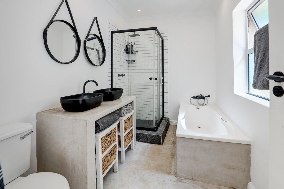 Modern bathroom featuring a concrete vanity with dual vessel sinks, a glass-enclosed shower with subway tiles, and a built-in bathtub.