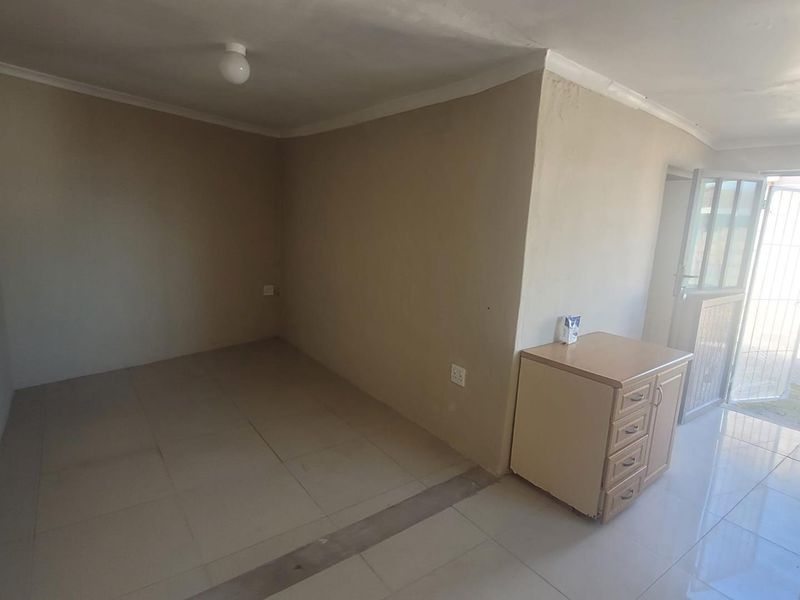 An empty living area featuring tiled flooring, neutral walls, and direct access to the exterior through a security gate.