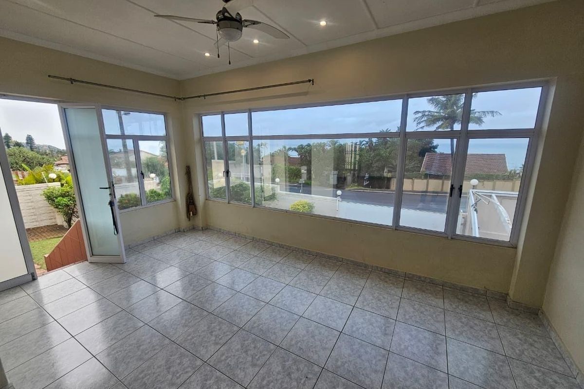 A bright, empty living area featuring large aluminium-framed windows, tiled flooring, and a ceiling fan, offering a spacious and airy atmosphere.