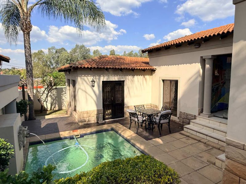A well-maintained outdoor pool area featuring a swimming pool with a water feature, wooden decking, and stone-clad exterior walls under a terracotta tiled roof.