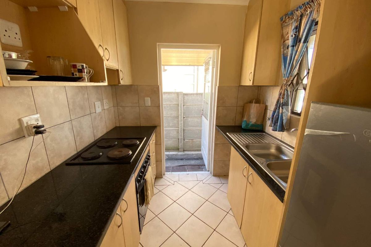Compact kitchen featuring built-in cabinetry, granite countertops, an electric hob, and a double bowl sink with direct access to the rear exterior.