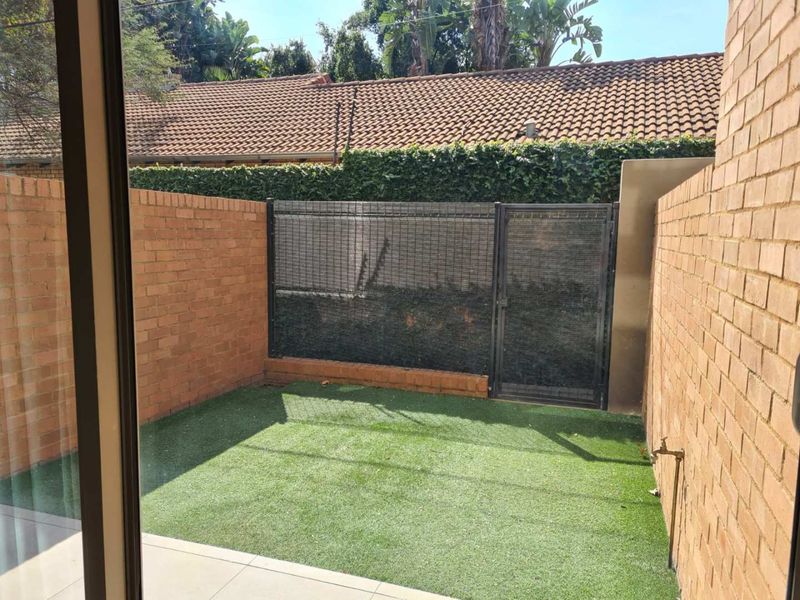 A private, low-maintenance courtyard featuring artificial turf, brick boundary walls, and a secure gate, accessible directly from the interior living space.