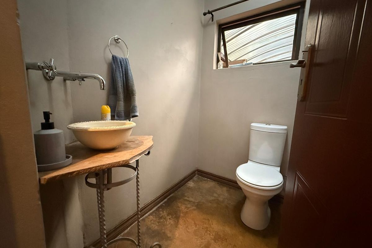 A compact guest bathroom featuring a pedestal-style basin, wall-mounted faucet, and a standard toilet with a small window for ventilation.