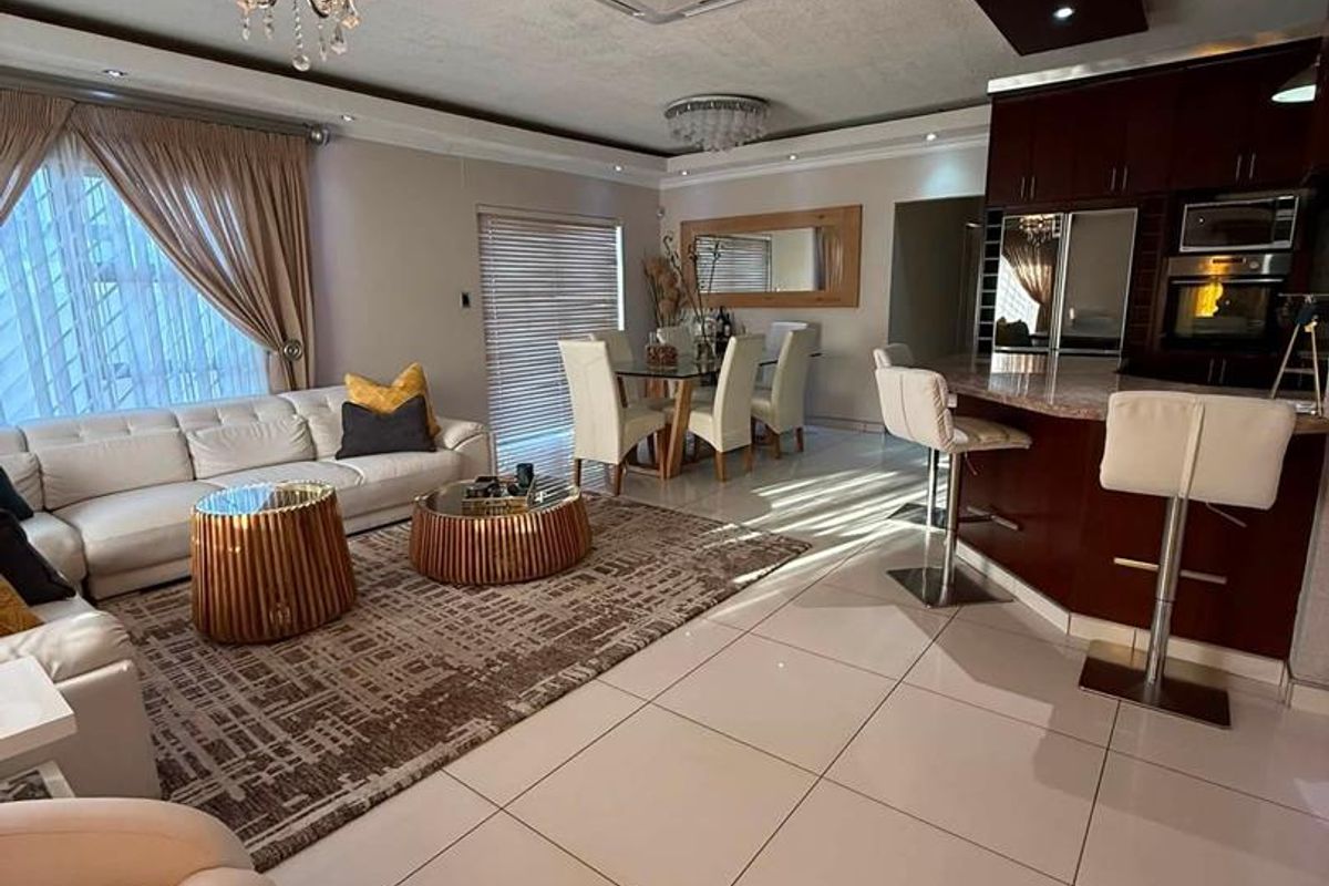 Spacious open-plan living and dining area featuring a modern kitchen with built-in appliances, breakfast bar, and sleek tiled flooring throughout.