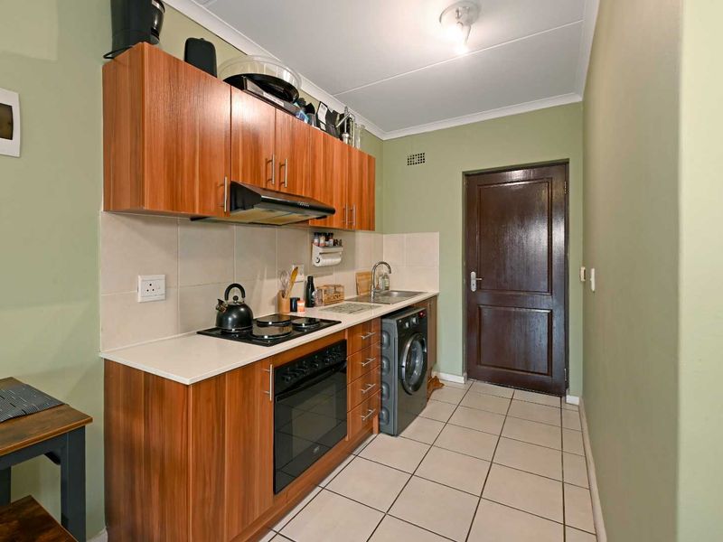 Compact kitchen featuring wood-look cabinetry, built-in oven with hob, extractor fan, tiled splashback, and integrated laundry plumbing.