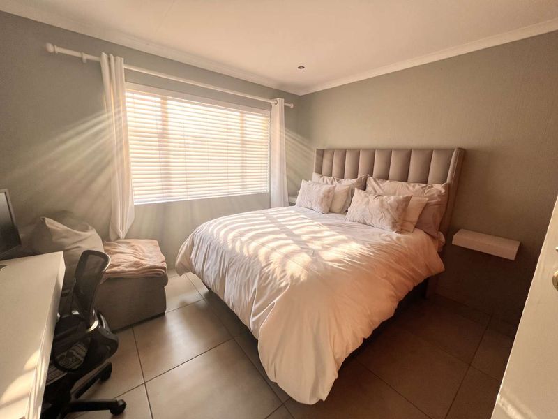 A well-lit bedroom featuring neutral wall tones, tiled flooring, and a built-in floating bedside shelf, creating a comfortable and functional living space.