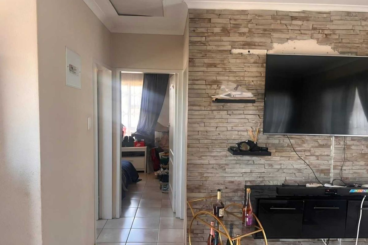 Living area featuring a stone-clad feature wall with visible damage, leading into a hallway and adjacent bedroom.