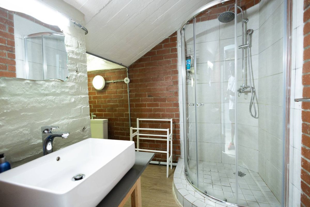 A bathroom featuring exposed brick walls, a curved glass shower enclosure with a rain shower head, and a modern vessel sink on a vanity.