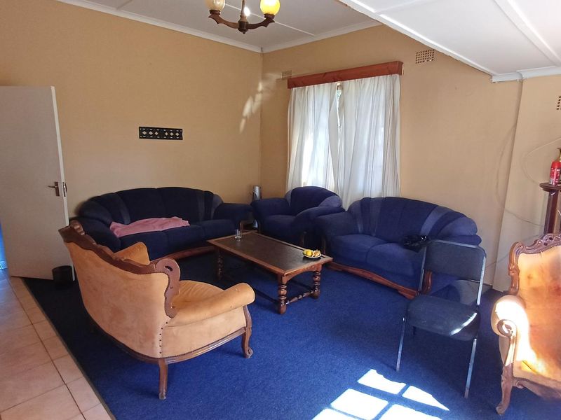 A dated living room featuring a combination of tiled and carpeted flooring, neutral wall tones, and a ceiling fan.
