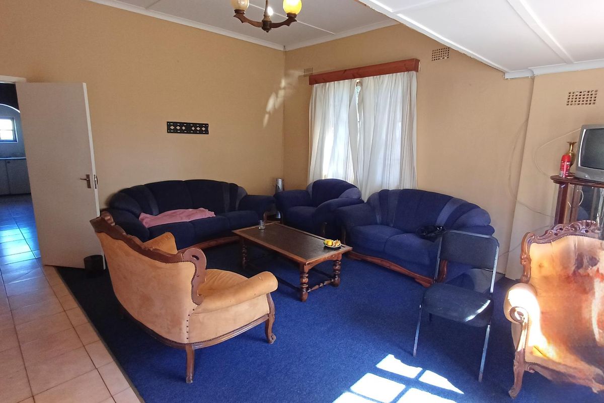A dated living room featuring a combination of tiled and carpeted flooring, neutral wall tones, and a ceiling fan.