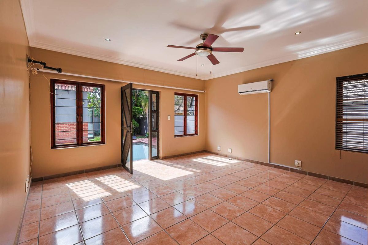 Spacious living room featuring tiled flooring, a ceiling fan, wall-mounted air conditioning unit, and direct access to the outdoor pool area.
