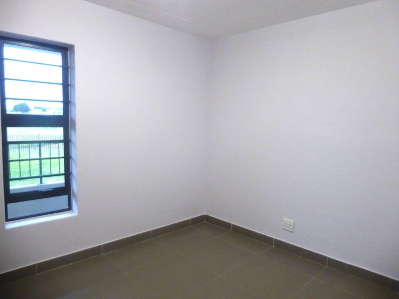 A clean, empty bedroom featuring neutral tiled flooring, white walls, and a window fitted with security bars.