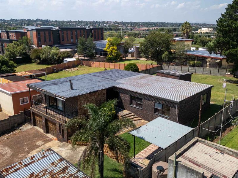 Aerial view of a detached house featuring a corrugated metal roof, brick and stone exterior, and a spacious surrounding garden with perimeter fencing.