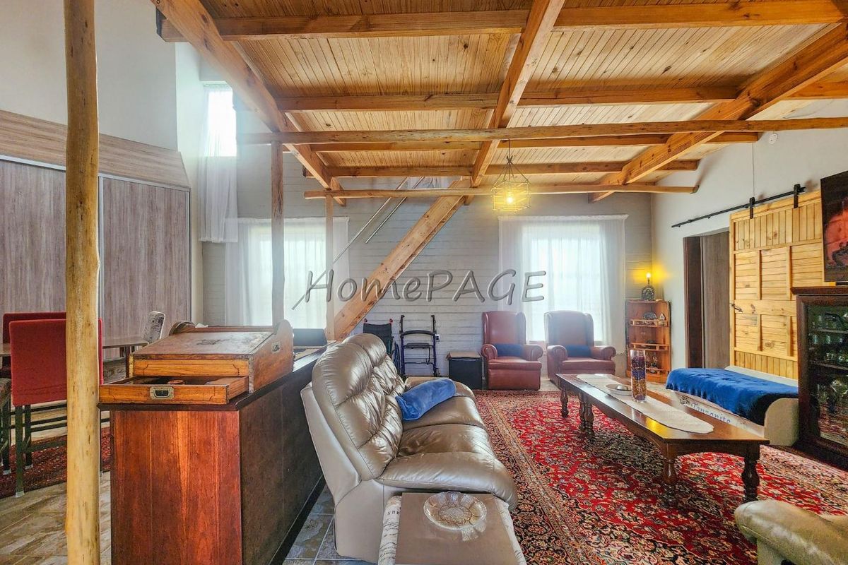 Spacious living area featuring exposed timber beam ceilings, a wooden staircase, and large windows providing ample natural light.