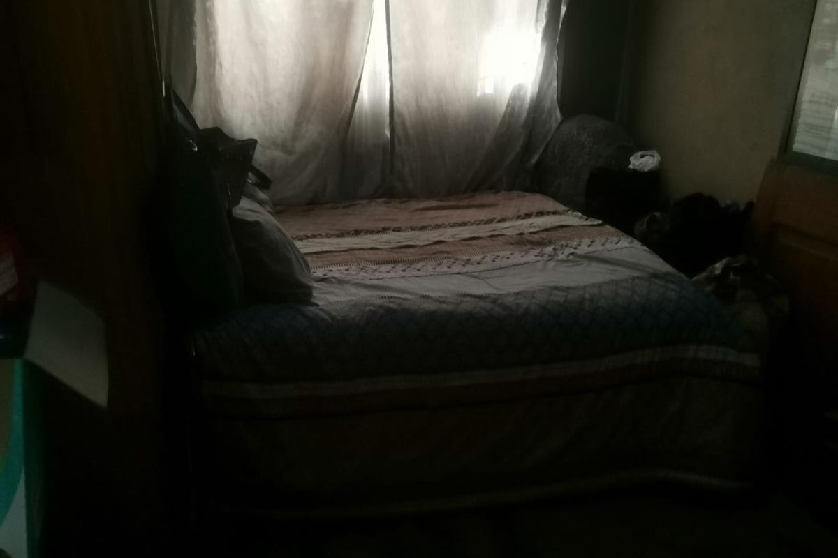 A dimly lit bedroom featuring a window with curtains, providing a basic sleeping space.