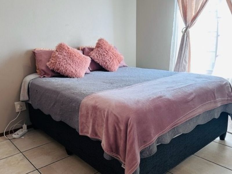 A bedroom featuring tiled flooring and a window with curtains, providing a functional and neutral space.