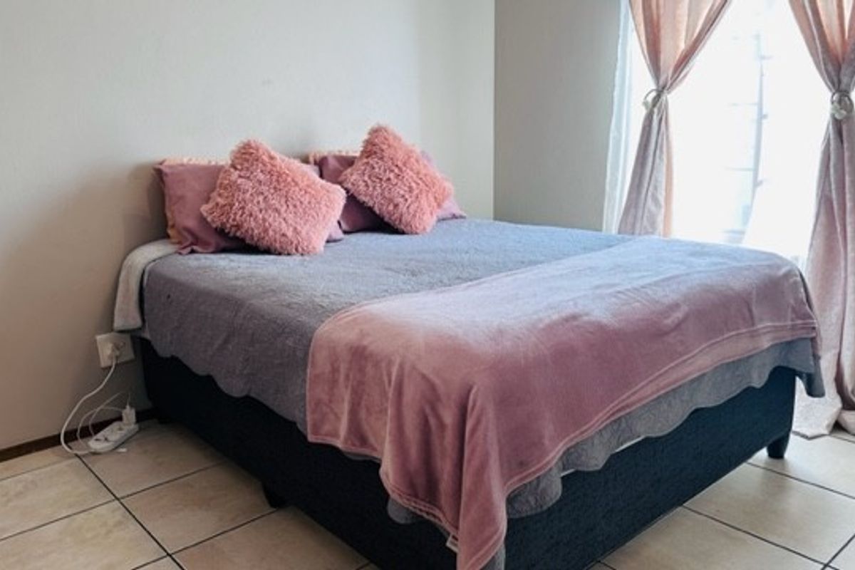 A bedroom featuring tiled flooring and a window with curtains, providing a functional and neutral space.