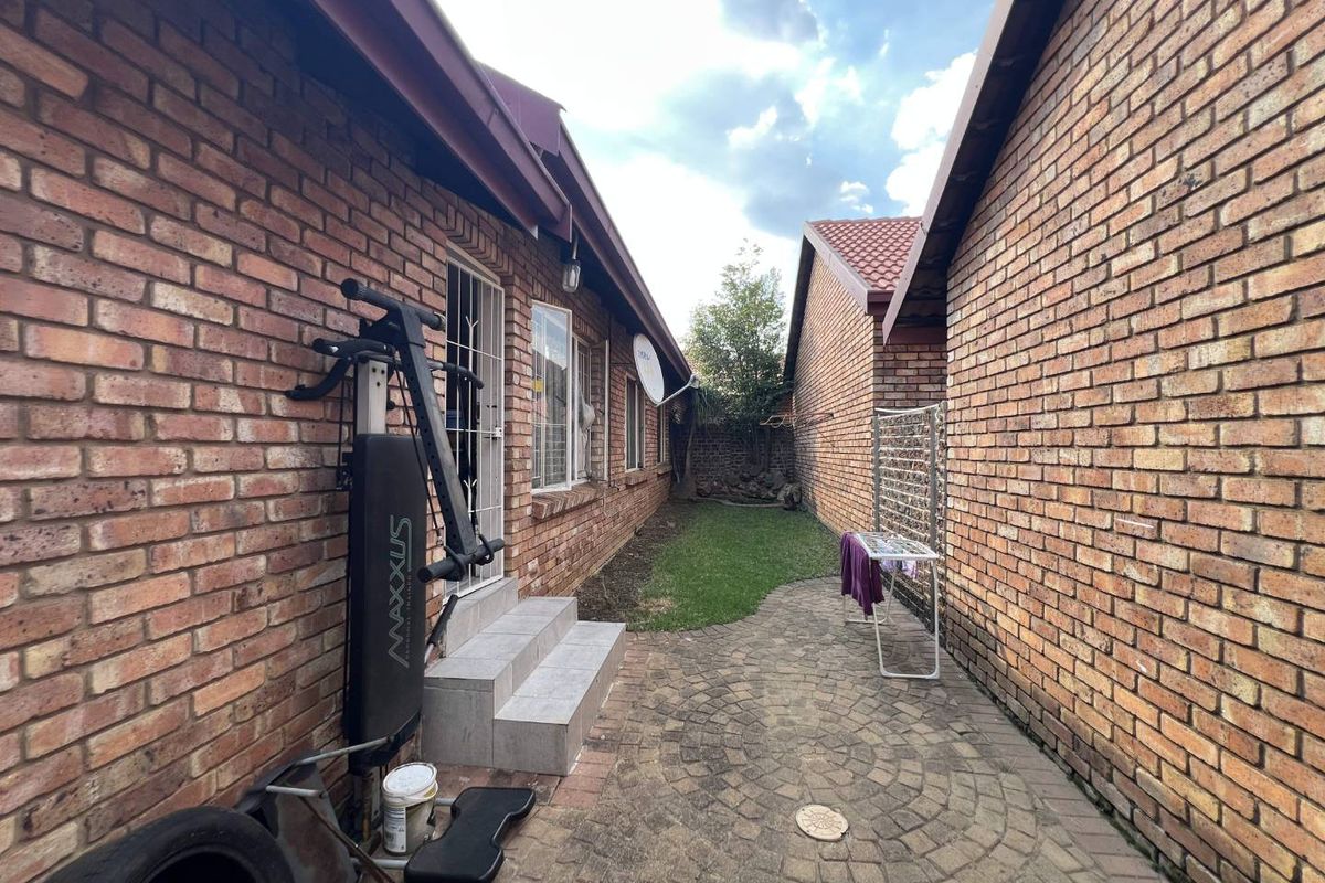 A side exterior view of the property featuring face brick walls, a paved walkway, and a small grassed area between two building structures.