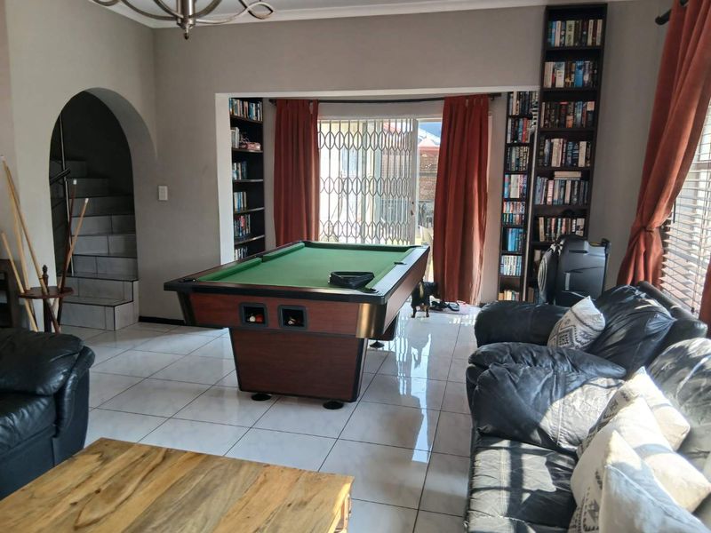 Spacious living area featuring tiled flooring, built-in bookshelves, and an arched entryway leading to a staircase, with direct access to the outdoor area.
