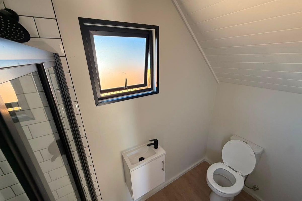 Modern bathroom featuring a shower enclosure with subway tiling, a wall-mounted vanity basin, and a toilet under a sloped ceiling.