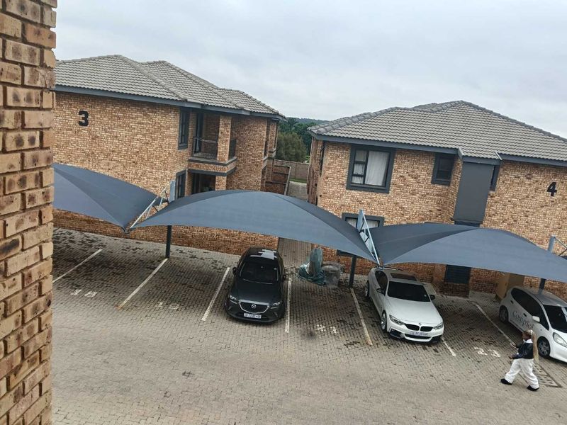 Exterior view of a townhouse complex featuring face brick buildings, tiled roofs, and covered parking bays with shade cloth structures.