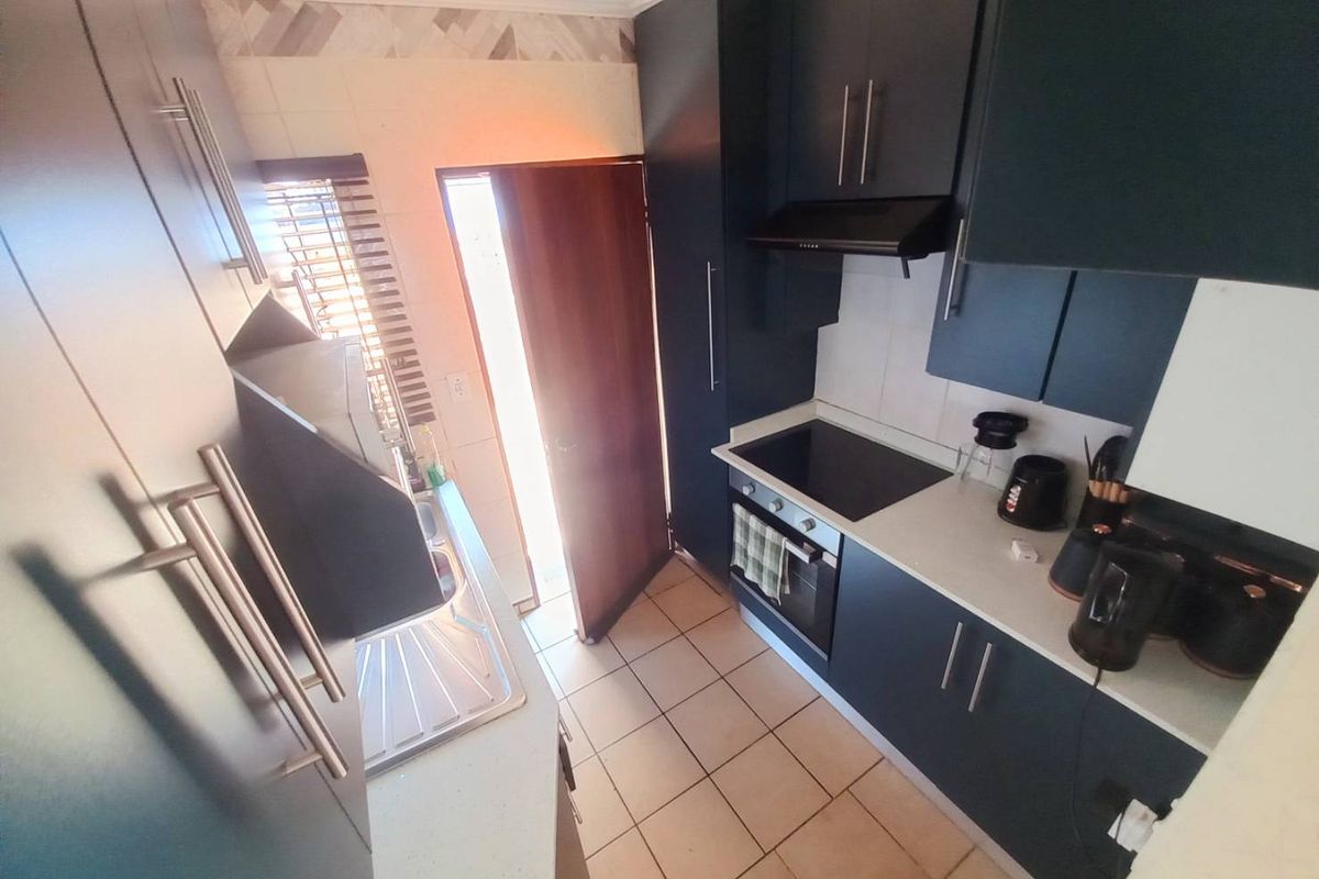 Compact galley-style kitchen featuring dark cabinetry, integrated oven, electric hob, extractor fan, and tiled flooring with direct access to the exterior.