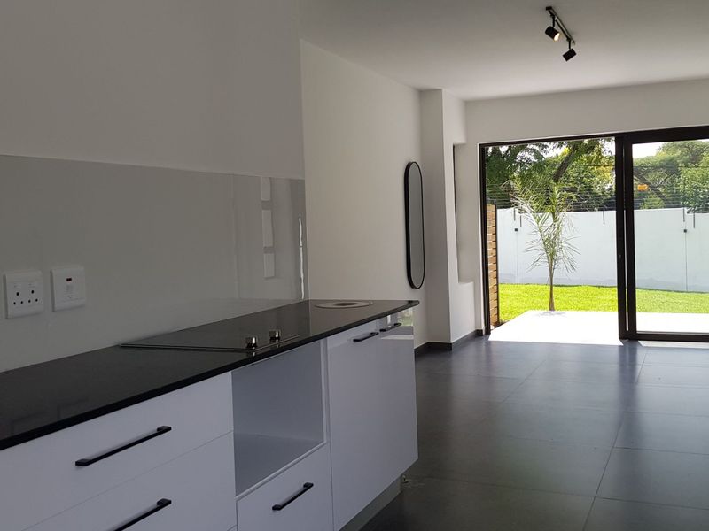 Modern open-plan kitchen area featuring sleek white cabinetry, dark stone countertops, and large sliding doors opening to a private garden.