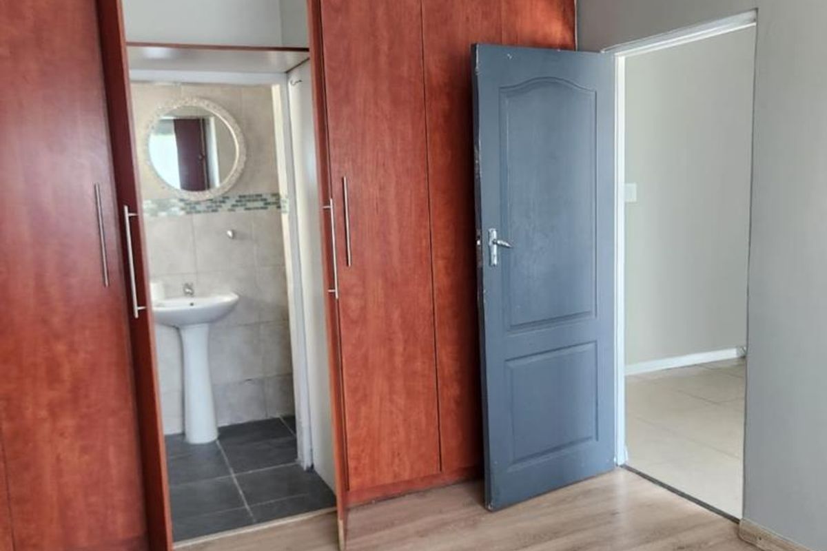 A spacious bedroom featuring laminate flooring, extensive built-in wooden cupboards, and direct access to an en-suite bathroom with a pedestal basin.