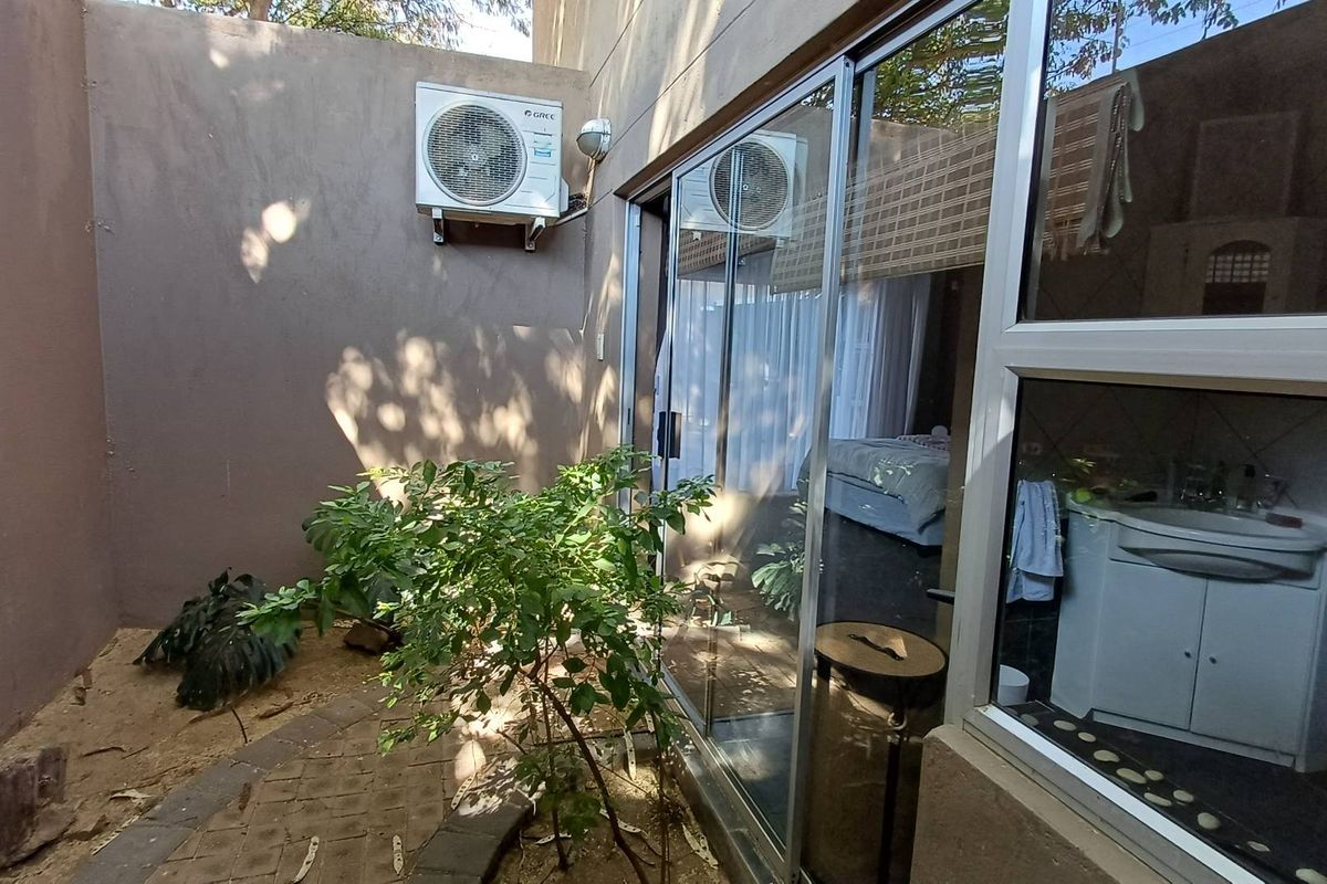 A private rear courtyard area featuring a paved walkway, boundary wall, and an external air conditioning unit, with views into the interior living space.