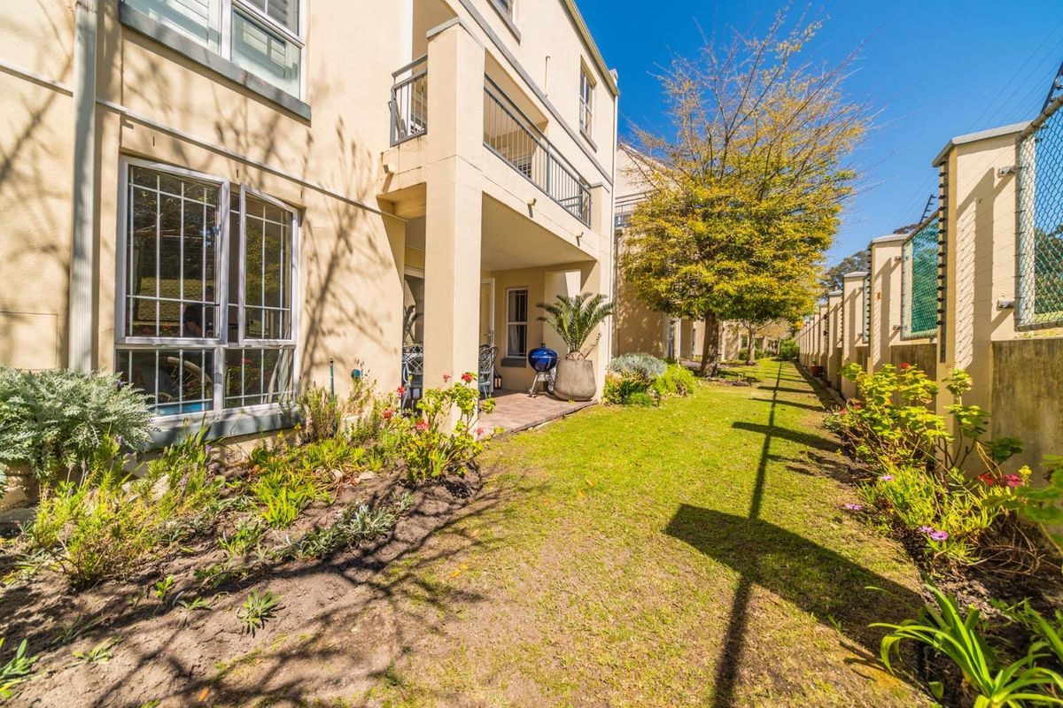 Rear view of the apartment building featuring a covered patio, landscaped garden area, and secure boundary walling.