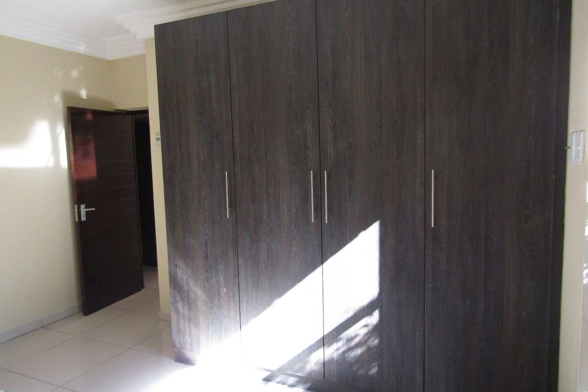 A bedroom featuring dark wood-grain built-in cupboards with modern handles and tiled flooring.