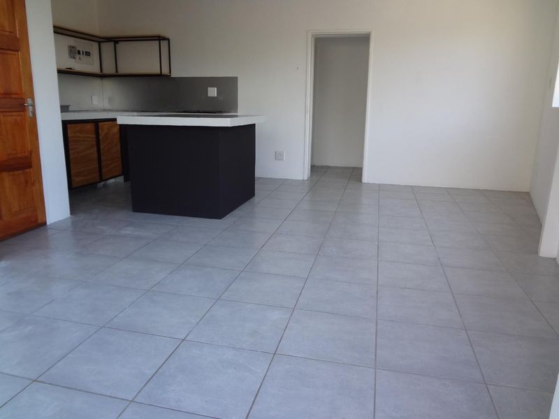 An open-plan living and kitchen area featuring modern grey floor tiles, a central kitchen island, and minimalist cabinetry.