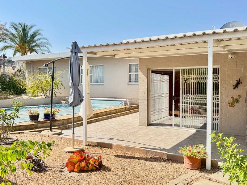 Outdoor patio area featuring a covered roof, built-in braai, and direct access to the swimming pool and garden.