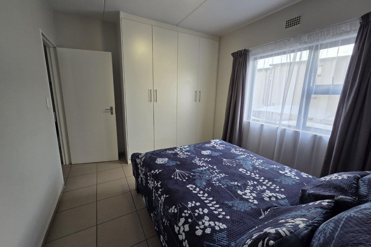 A functional bedroom featuring built-in floor-to-ceiling wardrobes, tiled flooring, and a window providing natural light.