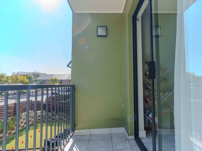 A private balcony featuring tiled flooring, a metal balustrade, and sliding glass door access, overlooking the complex grounds.