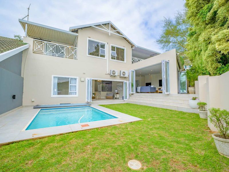 Rear view of the townhouse featuring a swimming pool, manicured lawn, raised patio area, and large bi-fold doors opening into the living space.