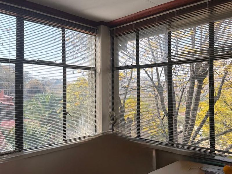 A bright, empty office space featuring large corner windows with venetian blinds, offering natural light and exterior views.