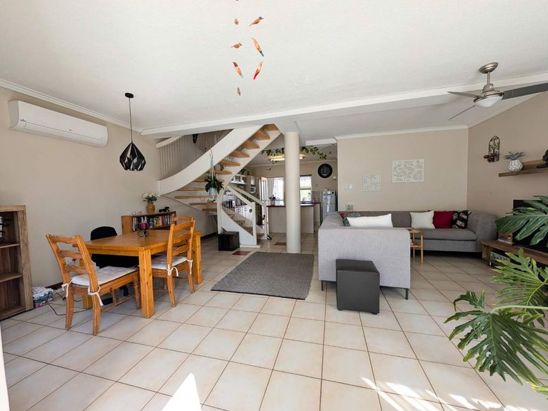 Spacious open-plan living and dining area featuring tiled flooring, a central staircase, and a split-system air conditioner for climate control.