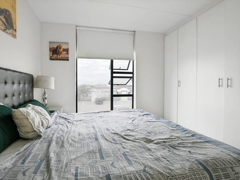 A well-maintained bedroom featuring built-in cupboards, neutral finishes, and a large window with a roller blind providing natural light.