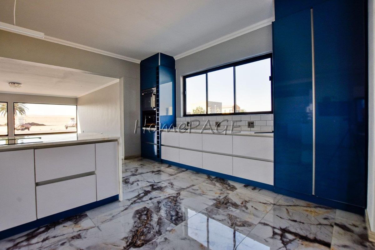 Modern kitchen featuring high-gloss blue and white cabinetry, marble-effect flooring, subway tile backsplash, and a central island, offering a clean and contemporary aesthetic.