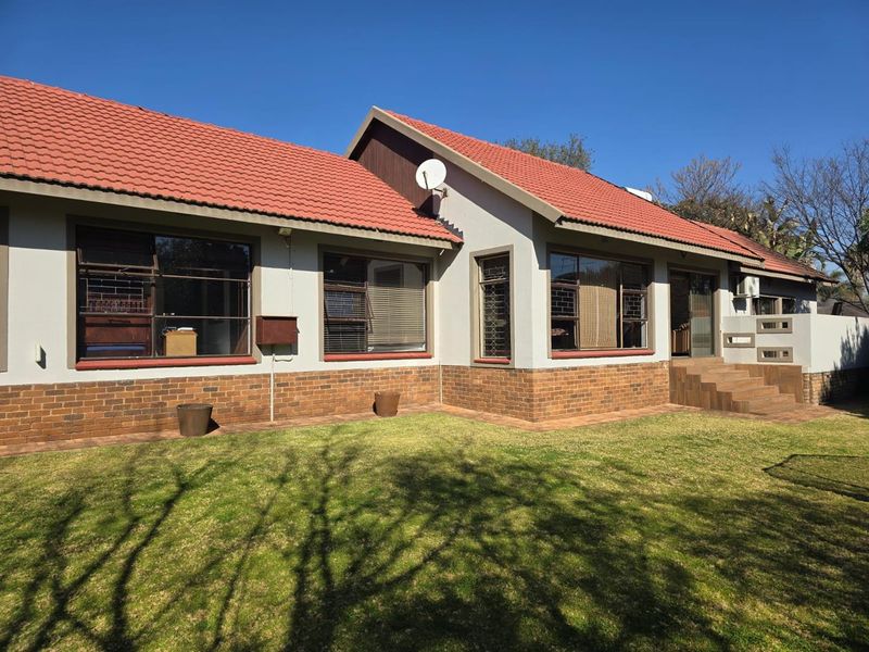 Rear view of the house featuring a tiled roof, brick base, and well-maintained lawn area with paved access steps.