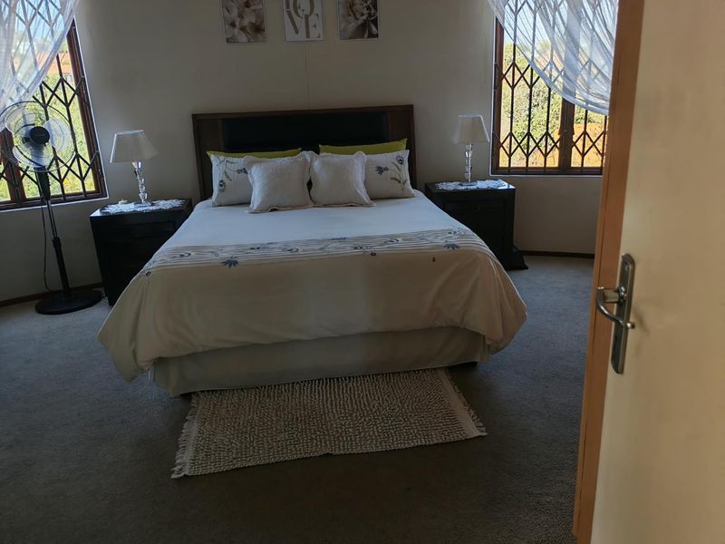 A carpeted bedroom featuring security bars on the windows and a built-in headboard, offering a functional and comfortable living space.