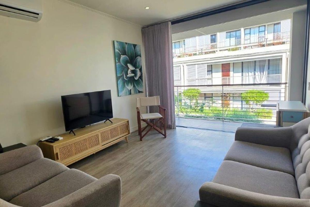 A bright living room featuring laminate flooring, a split-system air conditioner, and direct access to a private balcony through large sliding glass doors.