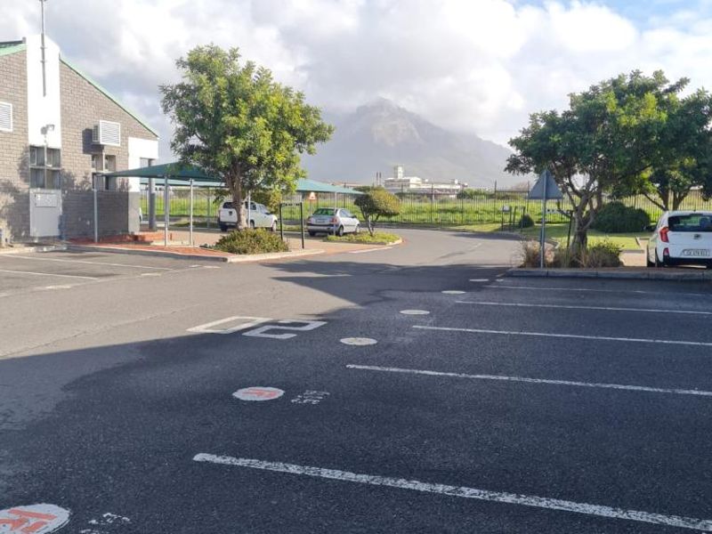 Exterior view of an office property featuring an asphalt parking area with marked bays, shade cloth carports, and perimeter fencing.