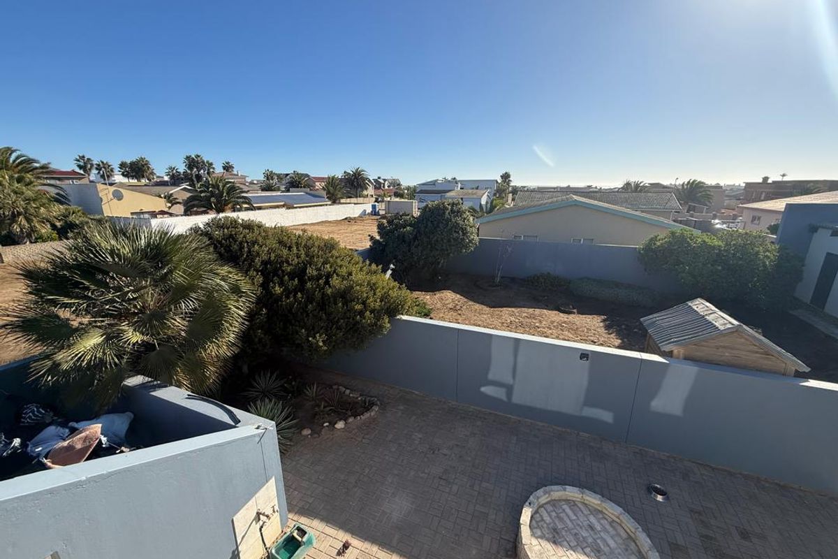 Elevated view of a rear garden featuring paved patio area, perimeter boundary walls, and established landscaping in a residential setting.