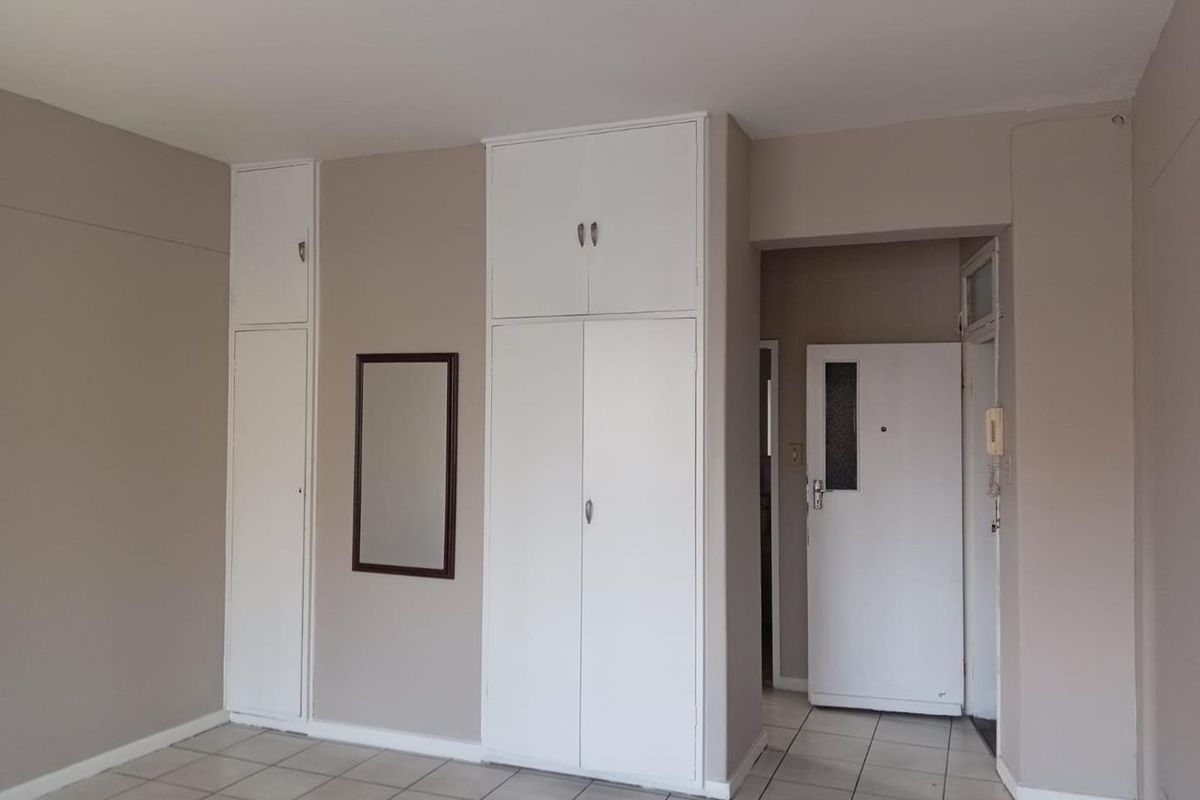 A clean, empty bedroom featuring neutral walls, tiled flooring, and ample built-in cupboard storage space.