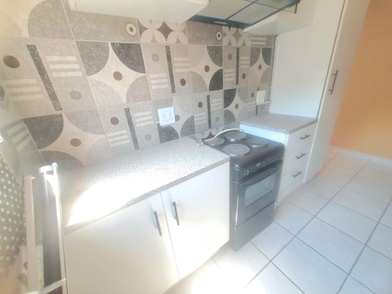 Compact kitchen featuring built-in cabinetry, laminate countertops, a tiled backsplash, and a freestanding electric stove with an overhead extractor fan.