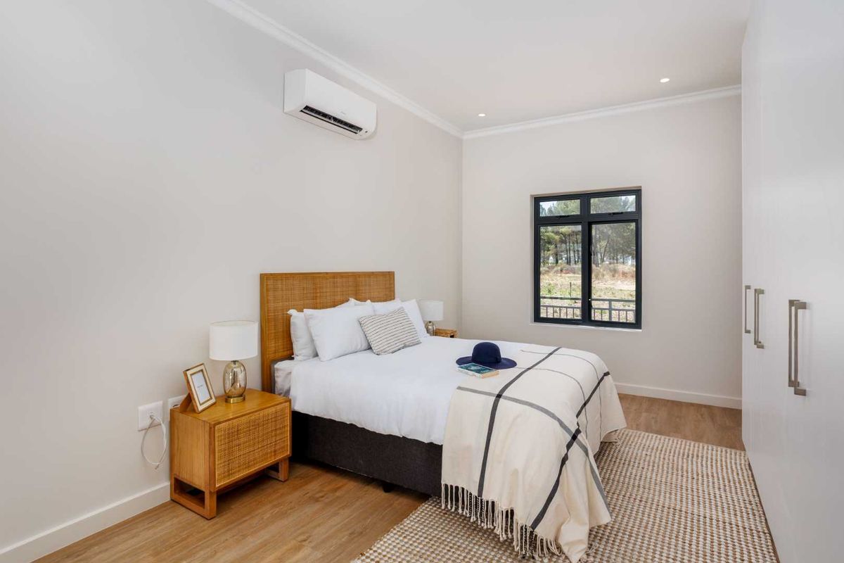 A well-maintained bedroom featuring timber-look flooring, built-in cupboards, recessed lighting, and a wall-mounted split-system air conditioner.